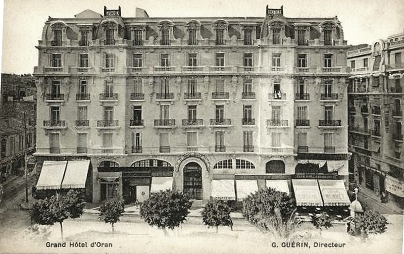 Carte postale photographique. Les mentions imprimées en pied donnent « Grand Hôtel d’Oran » et « G. Guérin, Directeur ». Stores déployés sur toute la longueur du rez-de-chaussée.