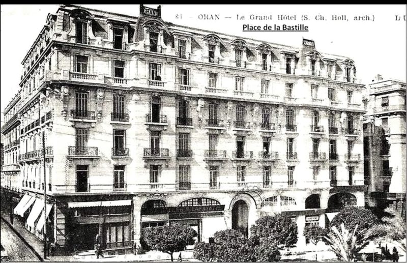 Vue de la façade complète, enseigne de toiture et commerces en rez-de-chaussée. La légende imprimée porte : « ORAN — Le Grand Hôtel (S. Ch. Holl, arch.) », et une mention manuscrite « Place de la Bastille ».