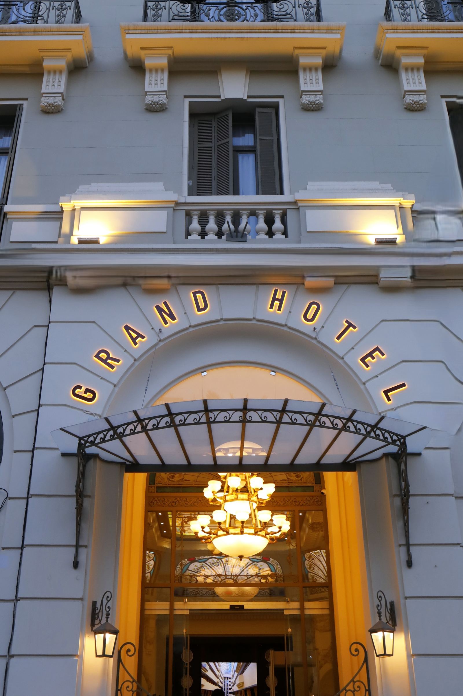 La même arcade aujourd’hui : auvent de fer, lettres dorées « Grand Hôtel », lustre et vitrail du sas visibles depuis la rue